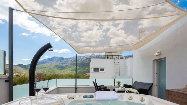 Un jacuzzi con vistas a la montaña, una zona de estar cubierta y un balcón con mesa y sillas.