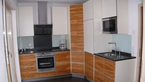 A compact kitchen with white cabinets, a microwave, a stove, and a coffee maker. - Feriendorf Uorsin Nr 8 by Interhome (Scuol)