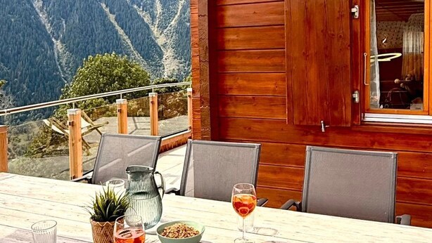 A wooden cabin with a dining table set for two, a pitcher, and a bowl of snacks. - Chalet Poiema by Interhome (Bellwald)
