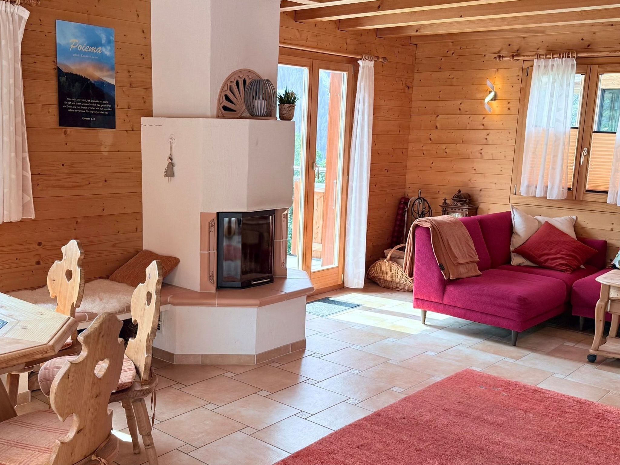 L’intérieur chaleureux d’un chalet, avec un revêtement mural en bois, une cheminée, un canapé rose et un coin repas doté de chaises en bois.