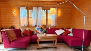 A cozy wooden cabin interior with a red sofa, a small wooden table, and a floor lamp. - Chalet Poiema by Interhome (Bellwald)