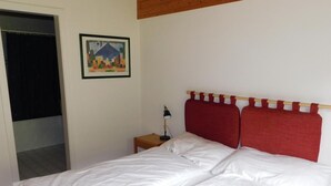 A bedroom with a bed, a nightstand, a lamp, a painting on the wall, and a door. - Residence Edelweiss A131 by Interhome (Bellwald)