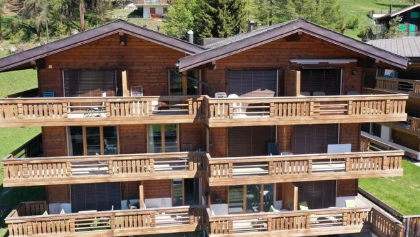A multi-story wooden chalet with balconies, large windows, and a mountainous backdrop. - Residence Edelweiss A131 by Interhome (Bellwald)