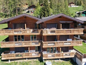 En storslagen chalet i trä med flera våningar, balkonger, stora fönster och en imponerande bergskuliss i bakgrunden.