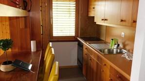 A compact kitchen with wooden cabinets, a sink, and a small window with blinds. - Residence Edelweiss A131 by Interhome (Bellwald)