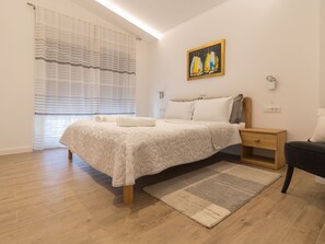 Ein Schlafzimmer mit Bett, Nachttisch, Stuhl, einem Wandbild und einem Fenster mit Vorhängen.