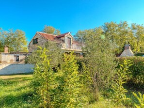 Une maison en pierre avec un toit recouvert de tuiles rouges, un balcon et une cheminée.