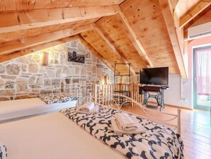 Une chambre confortable située dans les combles, avec un mur en pierre, des poutres en bois, un lit avec une literie à motifs, une télévision et une petite table.