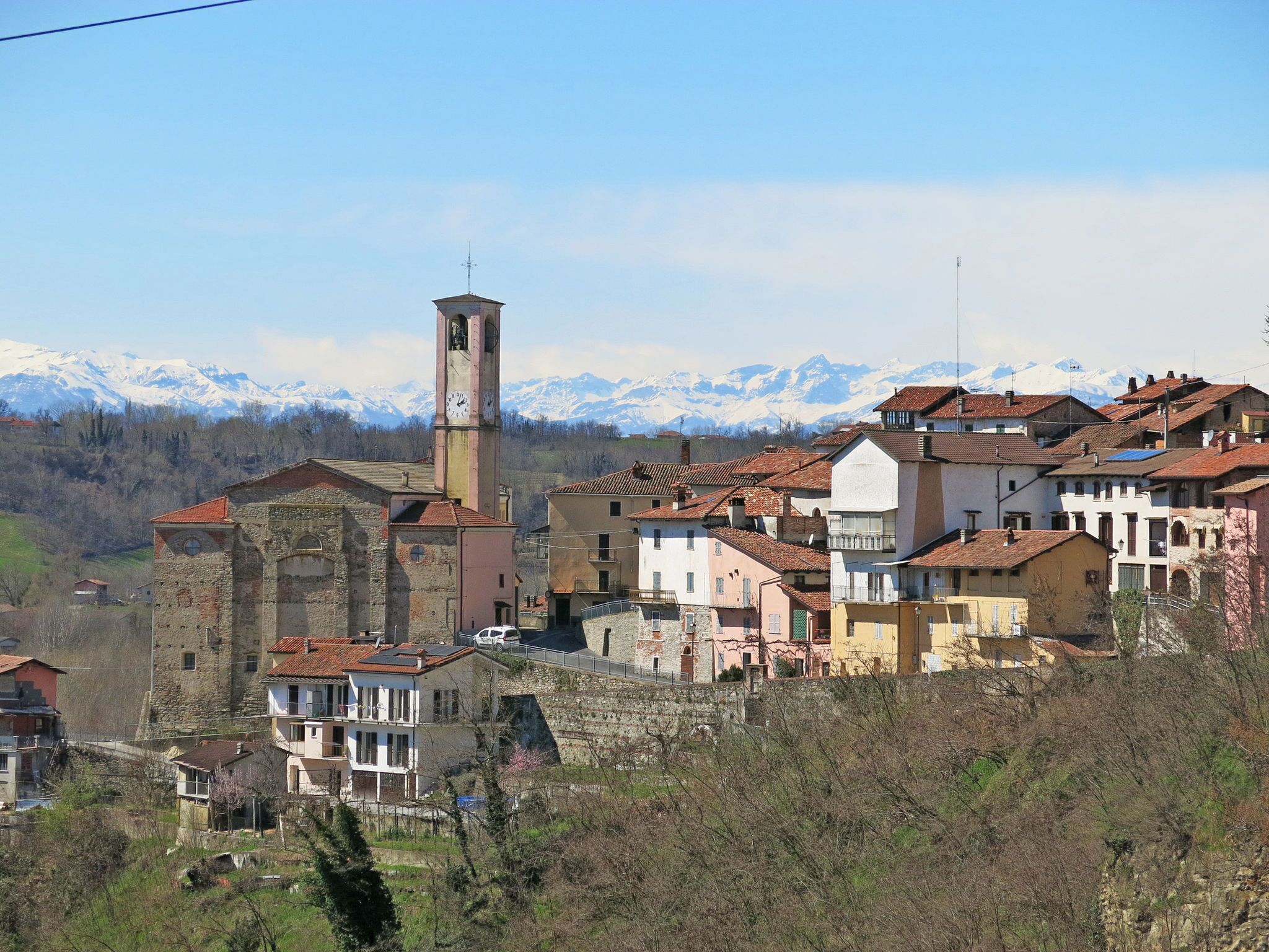 Un pueblo histórico con una destacada torre de reloj, edificios tradicionales y montañas nevadas al fondo.
