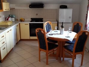 Eine kompakte Küche mit Essbereich. Sie beinhaltet ein Spülbecken, einen Herd, einen Geschirrspüler und einen Kühlschrank. Vier Stühle stehen um einen für das Essen gedeckten Tisch.