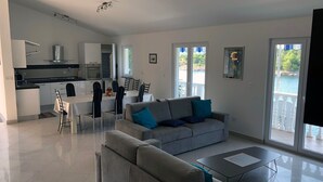 A modern living room with a grey sofa, a dining table with chairs, and a kitchen area with white cabinets and appliances. - Ferienwohnung by Interhome (Novigrad (Zadar))