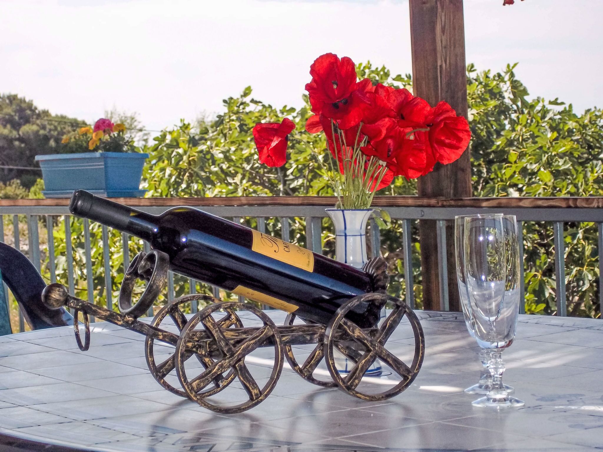 Een tafel met een wijnfles op een decoratieve wagen, een glas en rode bloemen in een vaas.