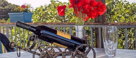 Een tafel met een wijnfles op een decoratieve wagen, een glas en rode bloemen in een vaas.