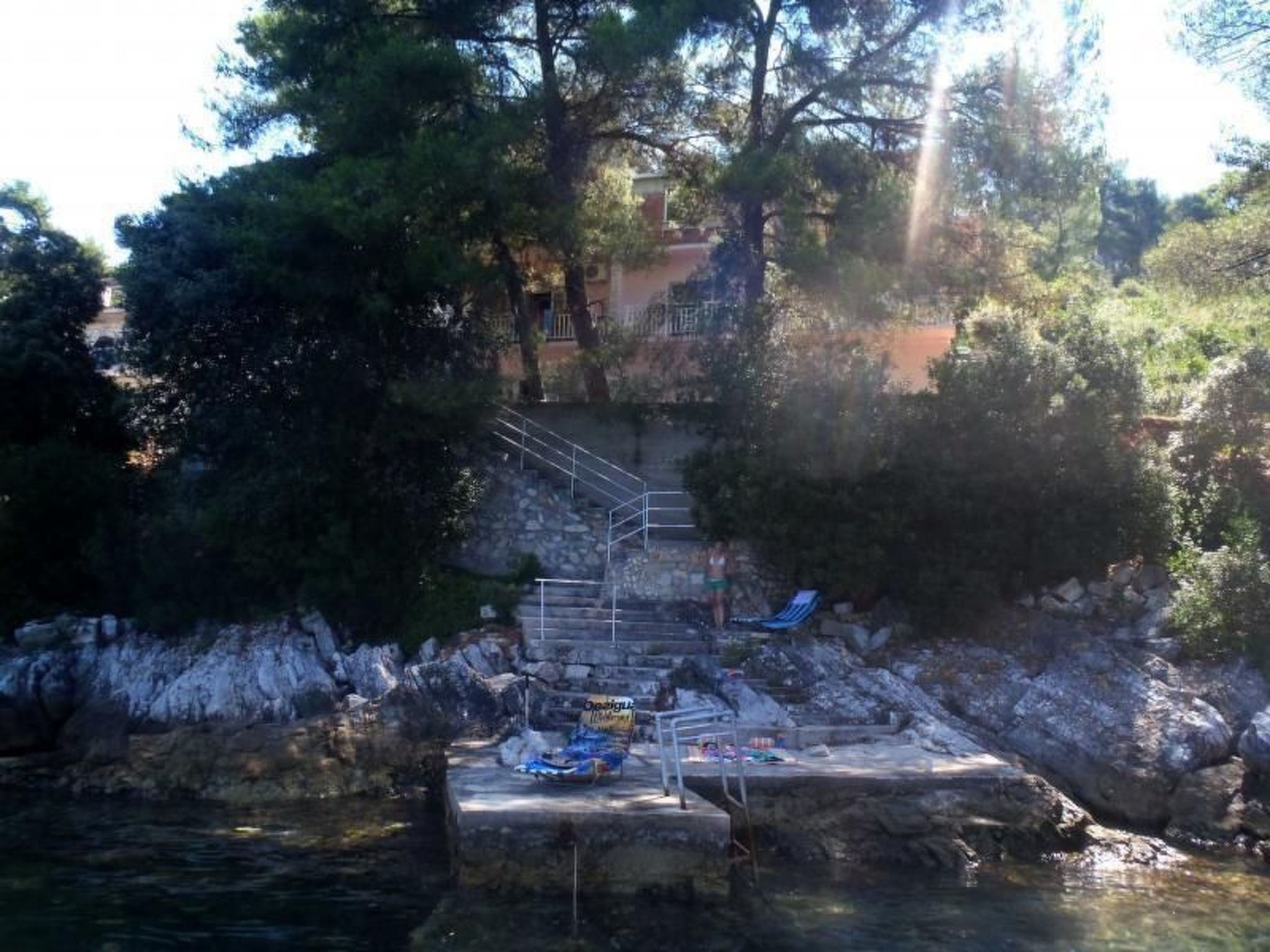 A stone pool with a metal staircase leading up to a building, surrounded by trees.
