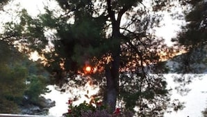 Ein weißer Tisch mit zwei Laternen und einer Blumenvase auf einem Balkon mit weißen Geländern, mit Blick auf ein Gewässer.