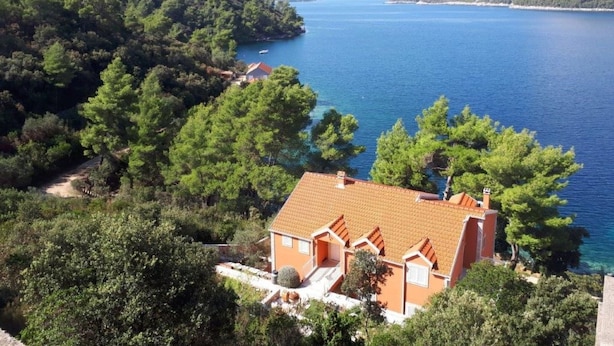Ein Küstenhaus mit Ziegeldach, umgeben von dichtem Grün und Blick aufs Meer.
