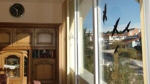 Ein Zimmer mit einem Holzschrank, einer Wanduhr und einem großen Fenster mit Blick auf Gebäude und Bäume.