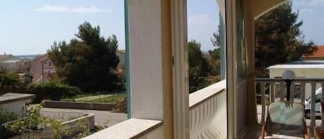 A balcony with a view of a residential area, a railing, and two wooden chairs.