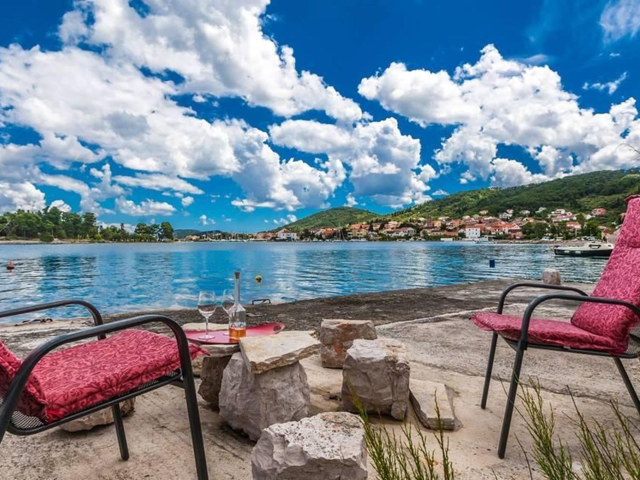 Une terrasse en bord de mer, avec des sièges en pierre, d’où l’on peut admirer un lac paisible et une ville lointaine.