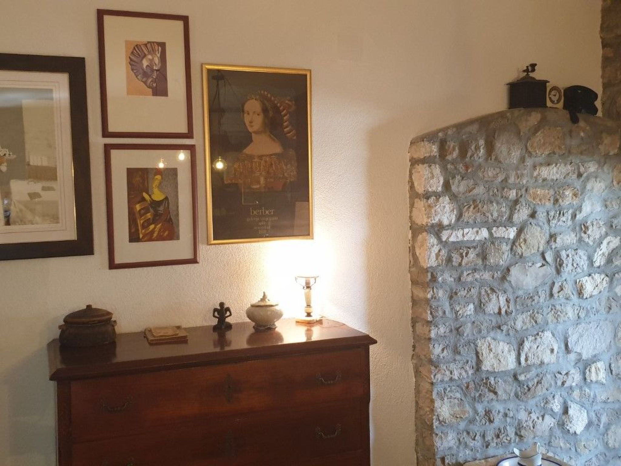 A room with a stone wall, a wooden dresser, and three framed pictures on the wall.