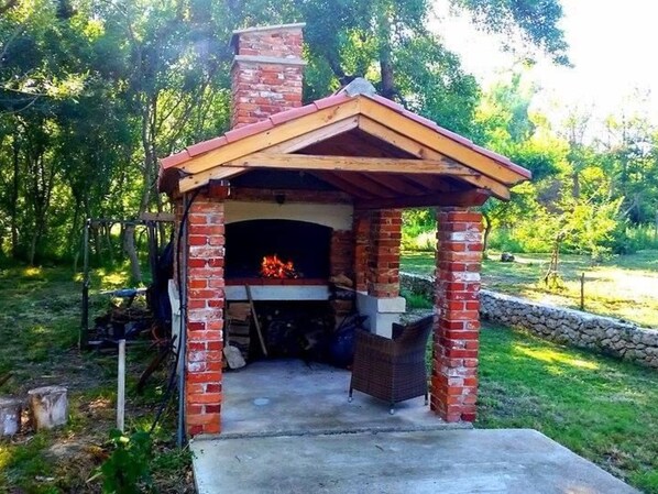 A brick-built outdoor fireplace with a wooden roof and a stone wall foundation. - Am Fluss gelegenes Haus mit Galerieschlafplätzen by Interhome (Nin)