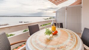 Una terraza con vista al mar, una mesa redonda con una botella y vasos, y mobiliario para exterior.