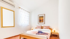Un dormitorio con una cama de madera, dos mesitas de noche con lámparas, un ventanal con cortinas y un cuadro enmarcado en la pared.