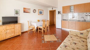 Un espacio habitable compacto con comedor, kitchenette y televisor sobre un mueble de madera.