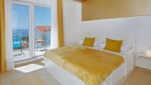 Een slaapkamer met een groot bed, een balkon met een tafel en stoelen, en uitzicht op zee.
