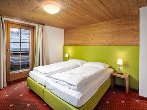 Un letto matrimoniale con due comodini, una finestra con tende e un soffitto in legno.