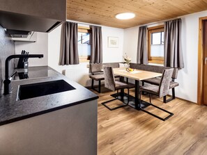 A modern kitchen with a built-in sink and a dining area with a wooden table and chairs. - Bio-Haus # 402 by Interhome (Neukirchen am Großvenediger)