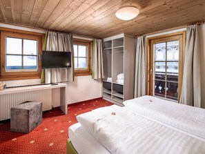 Ein Hotelzimmer mit einem Bett, einem Schreibtisch mit Fernseher, einem Kleiderschrank und einem Fenster mit Vorhängen.