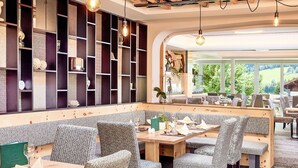 A restaurant with a long counter, patterned chairs, and a view of greenery outside. - Bio-Haus # 402 by Interhome (Neukirchen am Großvenediger)