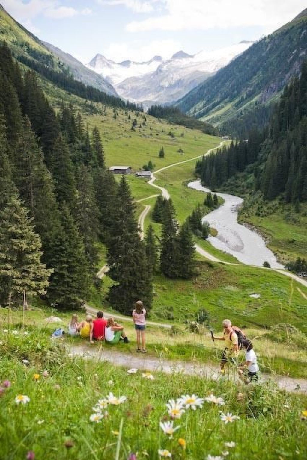 Un paisaje montañoso con un río, un sendero y personas apreciando la vista.