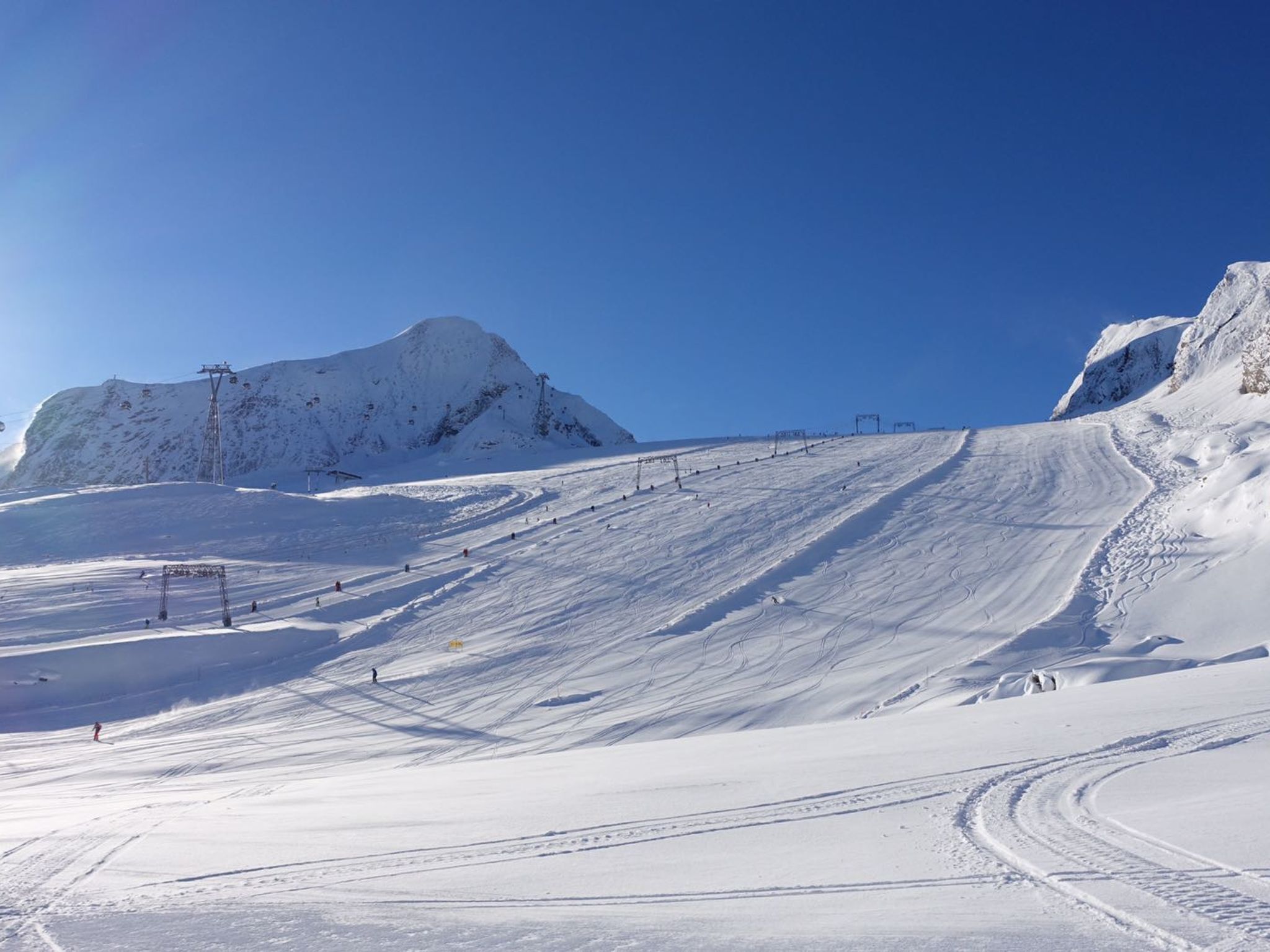 Une piste de ski enneigée, avec des remontées mécaniques, sous un ciel bleu dégagé.