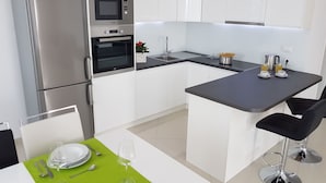 Une cuisine moderne avec des meubles blancs, un four encastré, un four à micro-ondes et un coin repas avec une table dressée pour deux personnes.