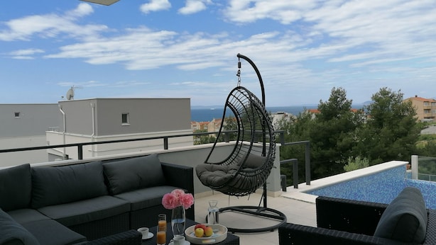Une terrasse sur le toit, aménagée avec un fauteuil suspendu, un canapé et une table à manger où sont disposés des fruits et des boissons.