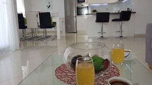 Une cuisine moderne équipée d’appareils électroménagers en acier inoxydable, un coin repas avec une table en verre et un espace de vie avec un canapé.