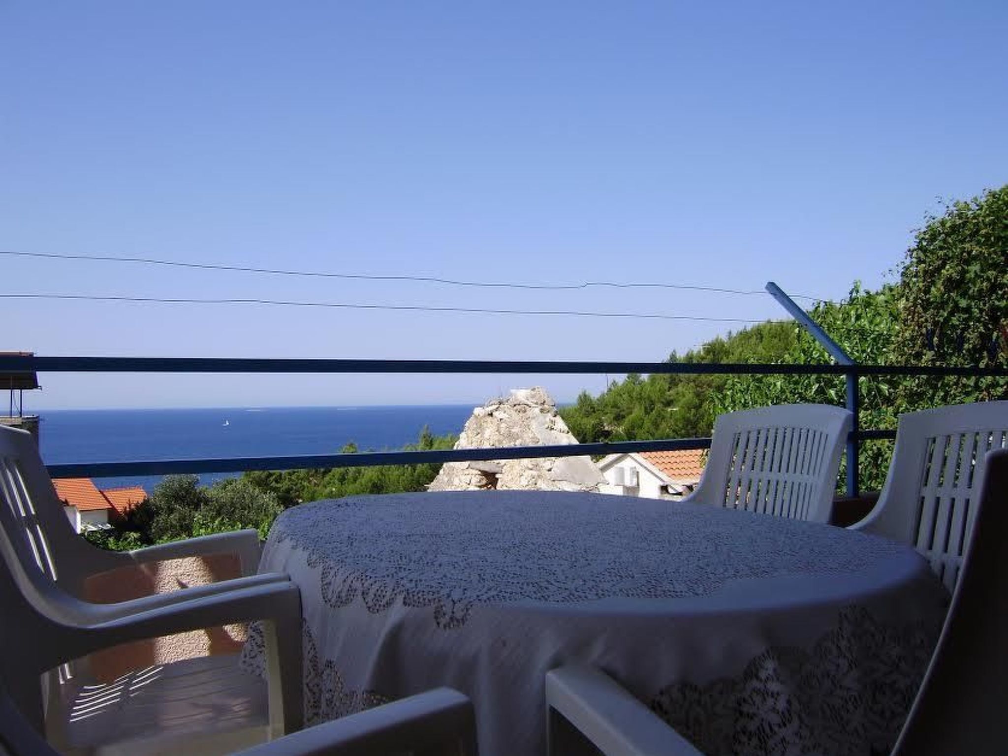Un balcon avec une table et des chaises, offrant une vue sur la côte et un ciel dégagé.