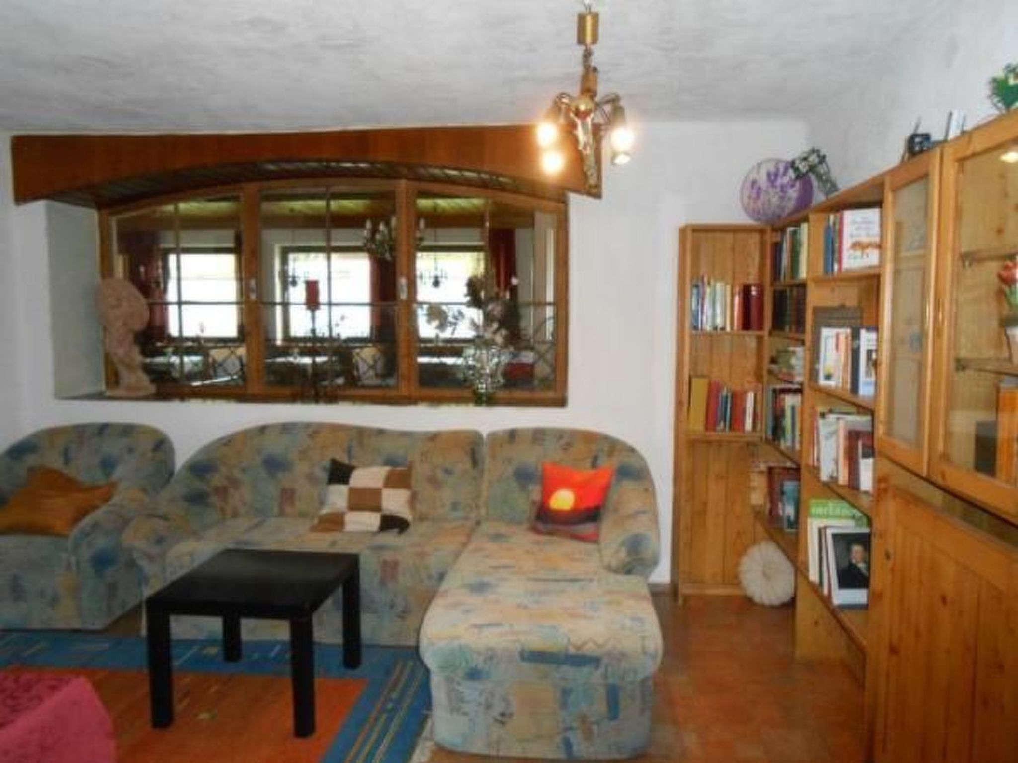 A cozy living room with a large window, a wooden bookshelf, and a patterned sofa.