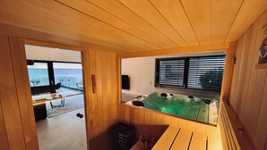 Un sauna de madera con banco, un jacuzzi y vista al mar a través de una ventana.