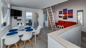 A modern living room with a red sofa, a dining area with white chairs and a table, and a TV mounted on the wall. - Wohnung "Olea Resort" mit Gemeinschaftspool by Interhome (Drvenik Mali)