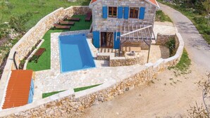 Una casa de pedra amb piscina, zona d'estar a l'exterior i mur de pedra que envolta la propietat.