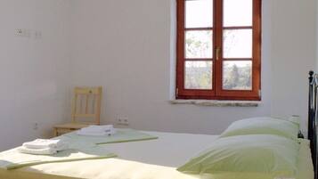 A bedroom with a single bed, a wooden nightstand, a lamp, and a window with a view of trees.