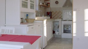 Cuina compacta amb armaris blancs, taula de dinar amb mantell vermell i lluminària penjant.