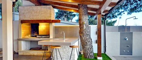 An outdoor kitchen with a stone countertop, bar stools, and a tree.