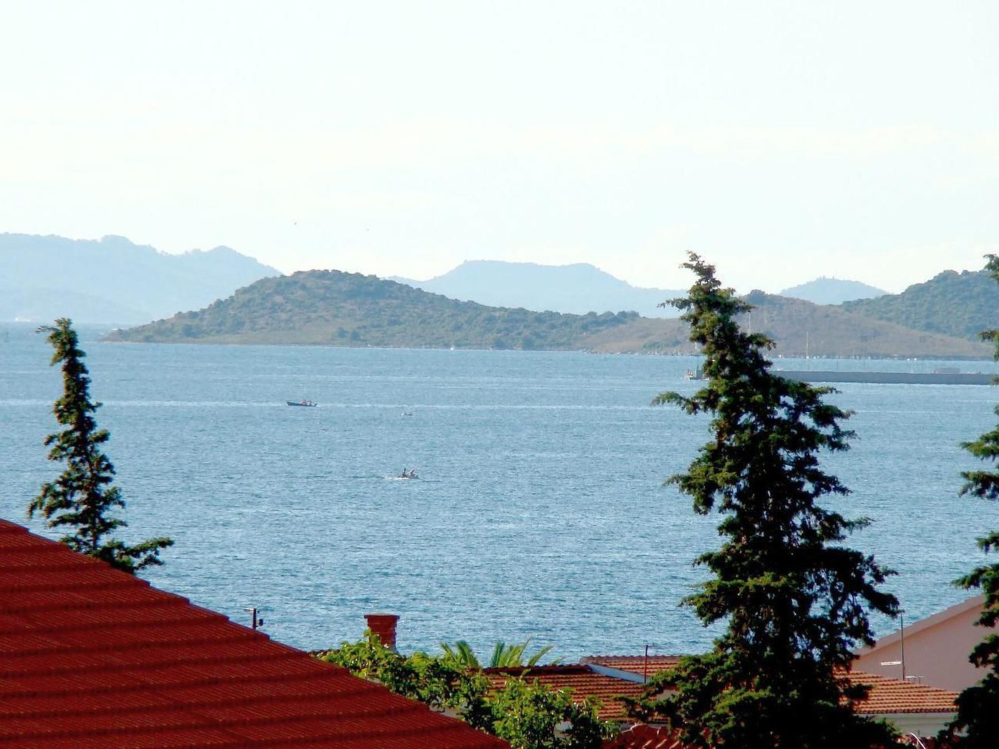 A coastal view with a body of water, distant hills, and a red-roofed building in the foreground.