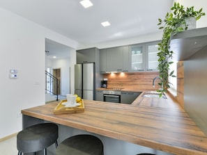 A modern kitchen with a wooden countertop, two black stools, a stainless steel refrigerator, and a potted plant. - Villa Vid 03 mit beheiztem Pool -TA Leut Agency by Interhome (Privlaka)