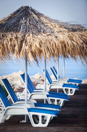 A row of white and blue lounge chairs under a thatched umbrella on a wooden deck by the sea. - Gemütliches, familienfreundliches Steinhaus by Interhome (Kolan)