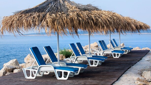 File di poltrone da spiaggia blu e bianche sotto un ombrellone di paglia, con vista su un mare calmo.